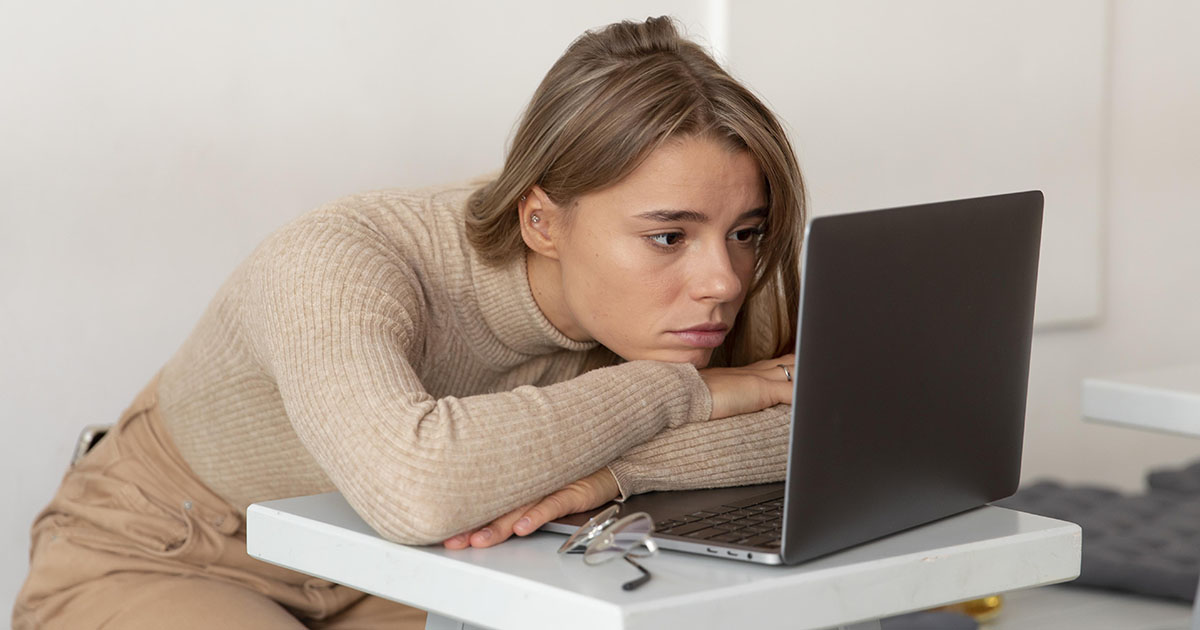 Amikor félbemarad az online marketing tanfolyam Szomorú nő ül a laptopja előtt, ráhajolva, az online marketing tanulás feladásának érzését jelképezve.
