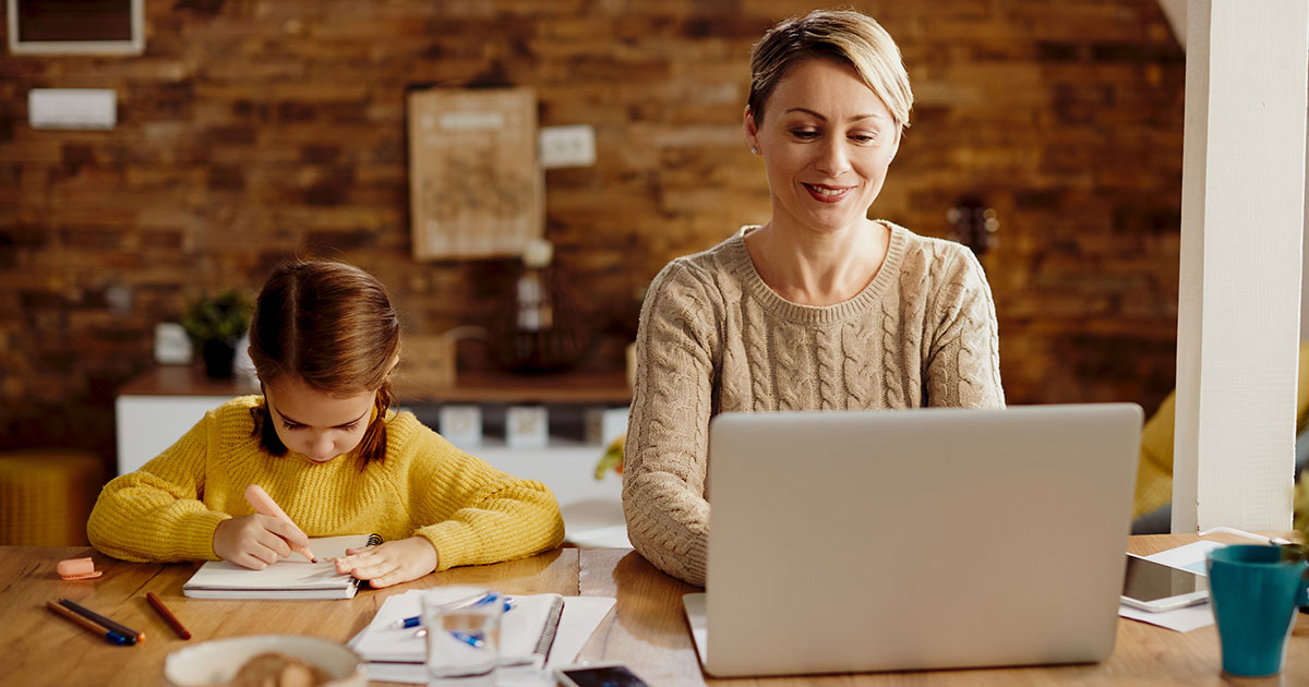 Online tanfolyam anyukáknak, tanulás gyerek mellett Egy anyuka mosolyogva online marketinget tanul a laptopja előtt ülve otthon, mellette játszó kisgyerekkel, az online tanulás rugalmasságát szimbolizálva.
